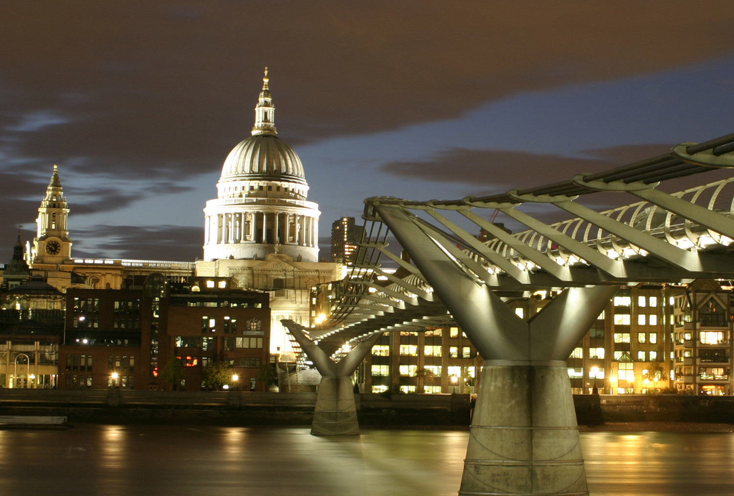 Viewed from The Tate Modern, the Millennium Bridge leads to an illuminated St Pauls Cathedral and London skyline.