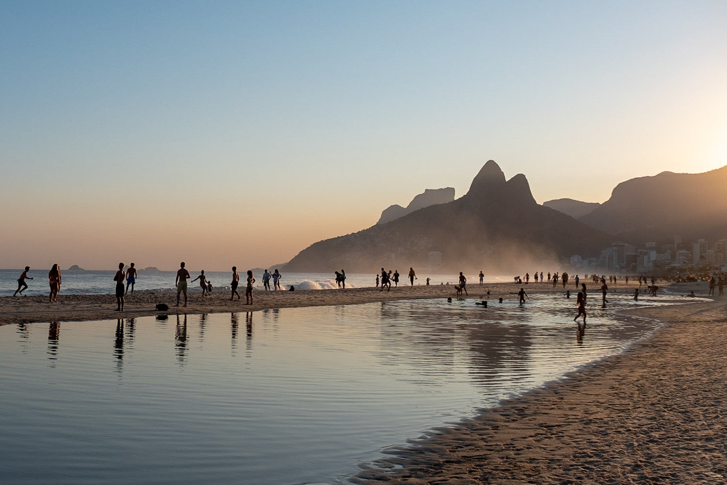 Silhouettes of beachgoers enjoying the sunset on Ipanema Beach, looking towards Twin brothers mountain in Rio de Janeiro, Brazil.