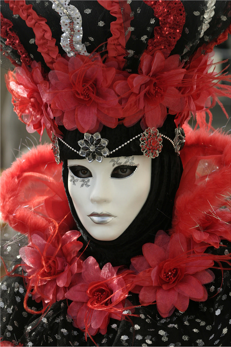 A lady in a white porcelain Venetian mask and vibrant red and black matching costume, taken at Venice Carnival in February.