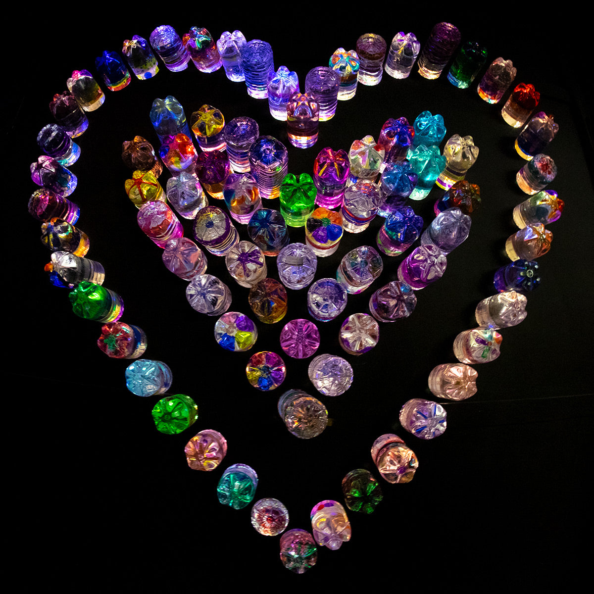 Photograph of an installation of plastic one litre bottles of coloured water and arranged as a colourful heart, at the London Lumiere. 