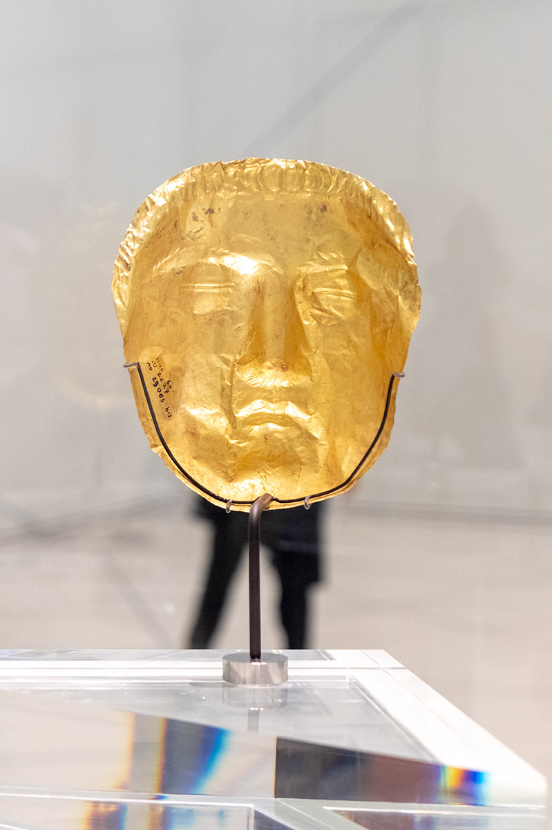 Funny placement of a gold face mask with the legs of a gallery steward standing behind it at The Louvre Museum, Abu Dhabi
