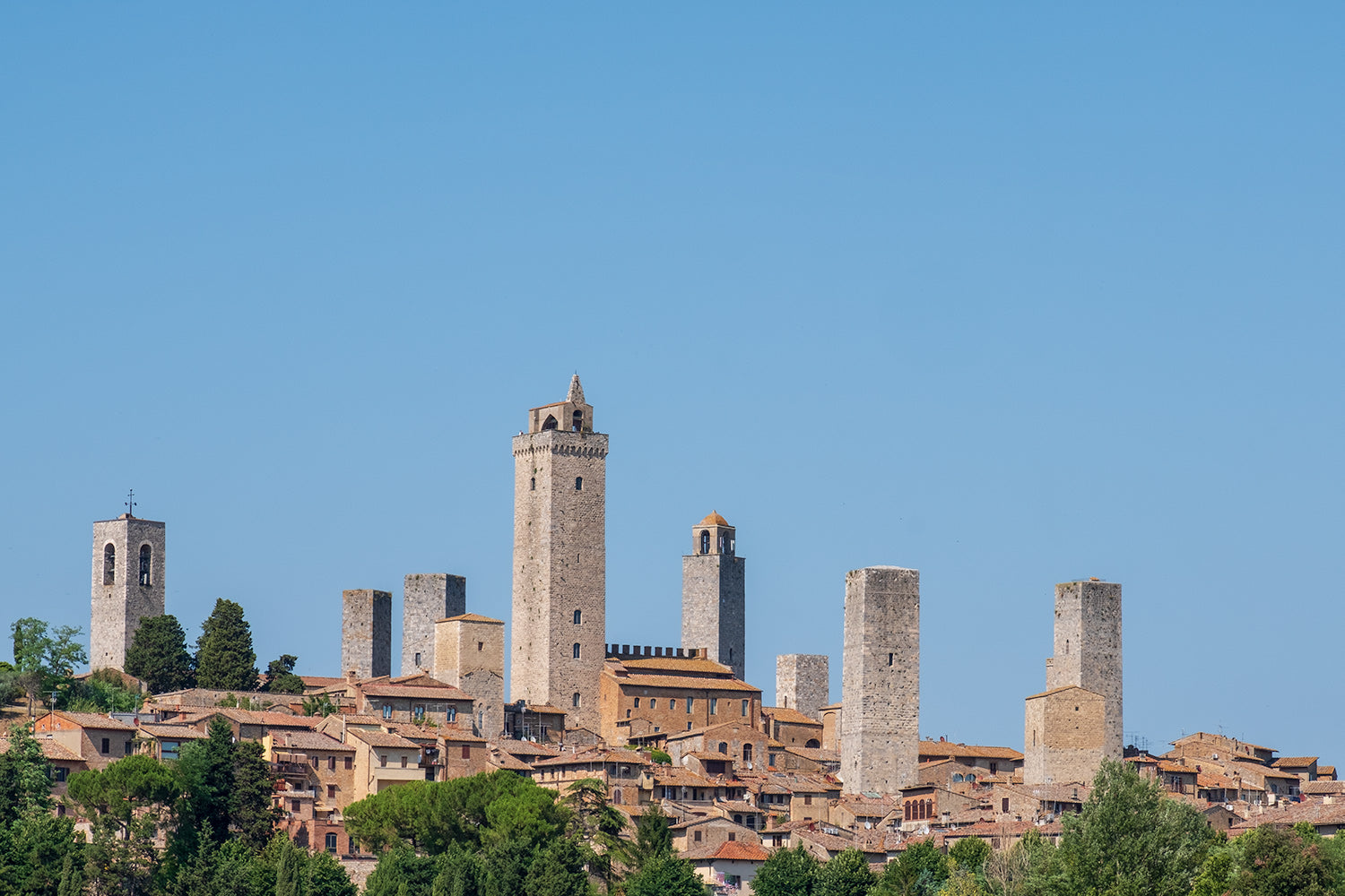 A clear blue sky behind the medieval town of San Gimignano in the province of Siena, Italy. A series of towers loom above the town.