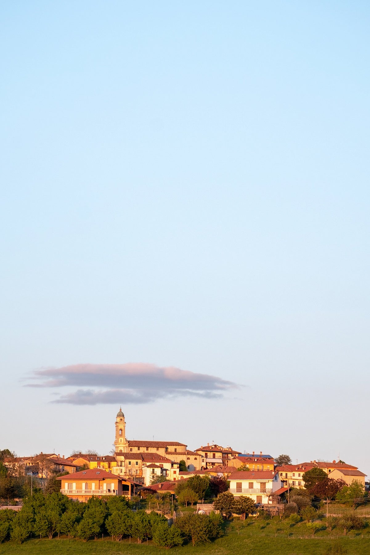 The hill top town of Roddino in Piedmont, early one evening in April. The sun shining on   the town with a light cloud formation and clear blue sky above.