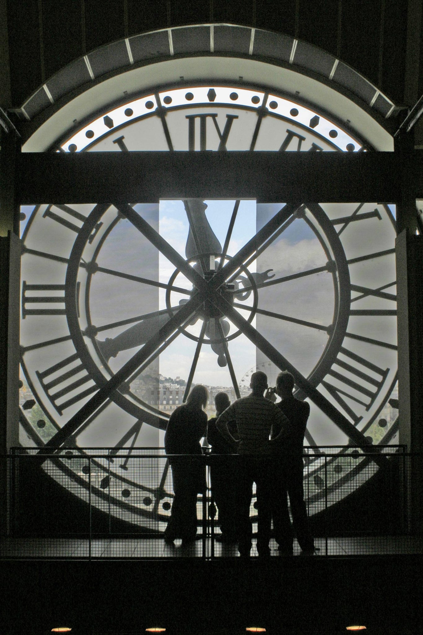 A silhouette of four people admiring the view of Paris, through a clock window at The Musee d'Orsay in Paris.