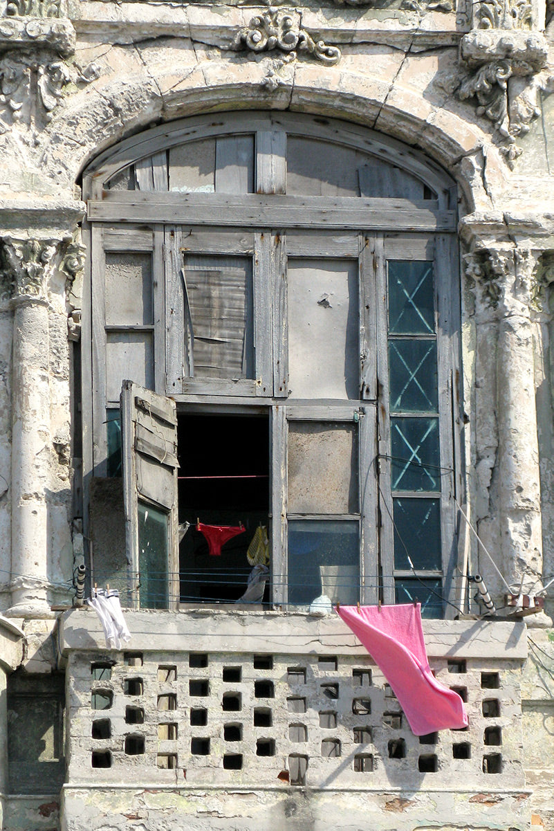 A pair of red knickers seen through a window and a pink towel waving over a balcony of a dilapidated building in Havana.	