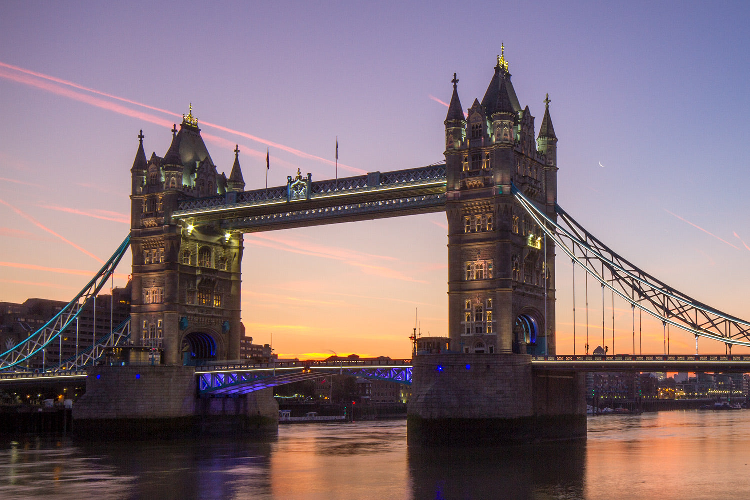 The dawn breaks over Tower Bridge and the River Thames as the sky changes colour to light purples and yellow.