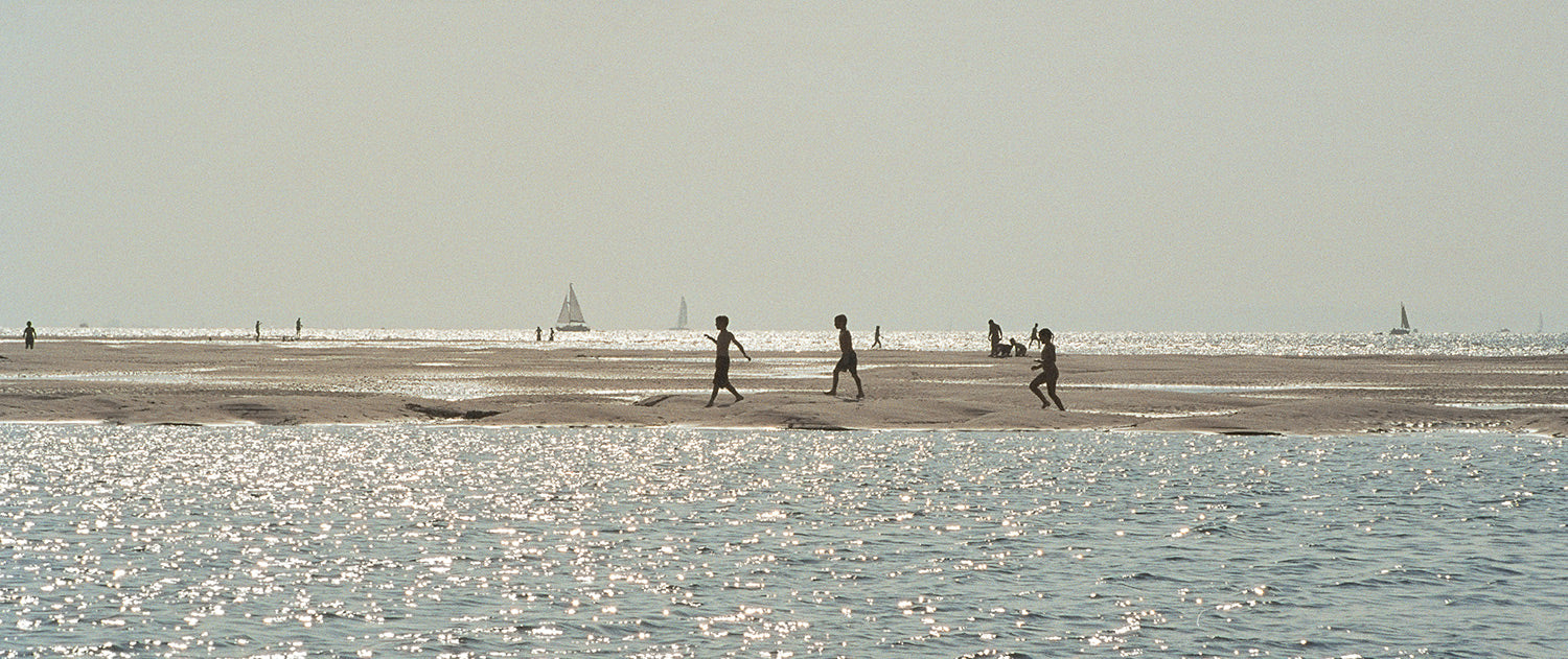 Three children in silhouette walking in a line between pools on the sands and the sea at West Witterings, East Sussex.