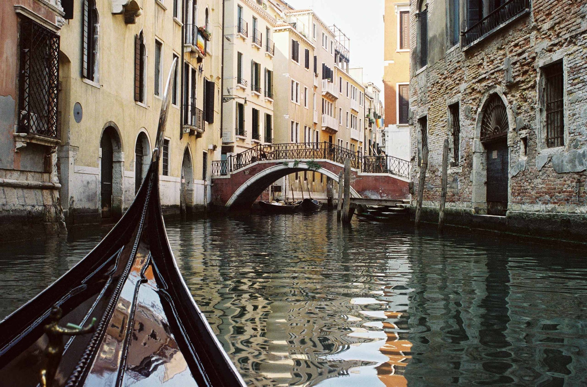 The front prow of a gondola points along the Venice canals as it travels towards the next bridge.